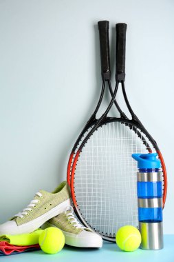 Tenis raketleri, toplar, giysiler, hafif arka planda su ve ayakkabı şişesi