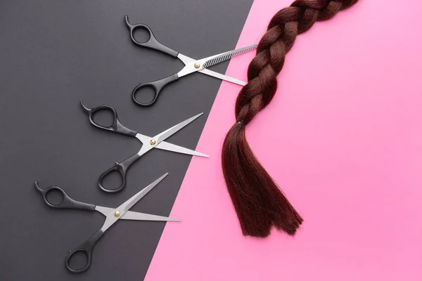 Braided hair strand and scissors on color background — Stock Photo, Image