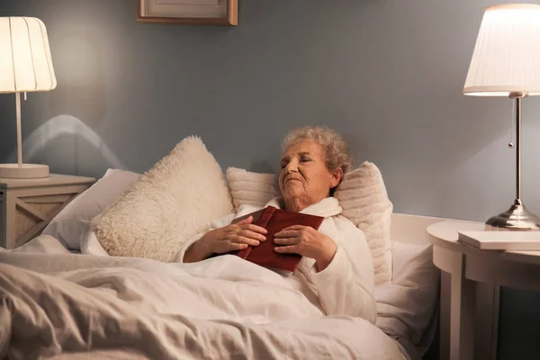 有书的老妇人晚上在床上睡觉 — 图库照片