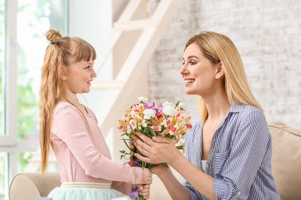 Klein meisje groet haar moeder met boeket van bloemen thuis — Stockfoto