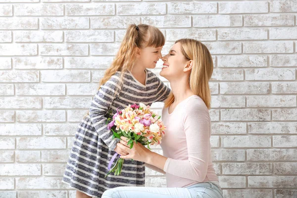 Little girl greeting her mother with bouquet of flowers against brick wall — Stock Photo, Image