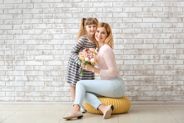 벽돌 벽에 꽃다발로 어머니를 맞이하는 어린 소녀 — 스톡 사진