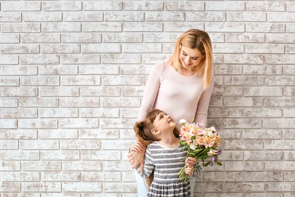 Little girl greeting her mother with bouquet of flowers against brick wall — Stock Photo, Image