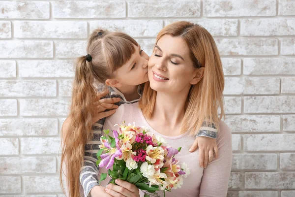 Bambina saluto sua madre con mazzo di fiori contro muro di mattoni — Foto Stock