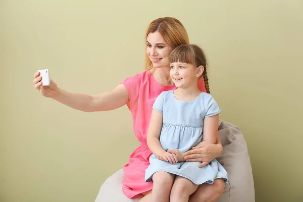 Little girl and her mother taking selfie on color background — Stock Photo, Image