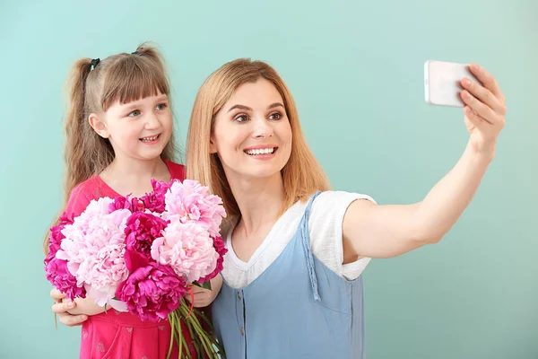 Little girl and her mother taking selfie with flowers on color background — Stock Photo, Image