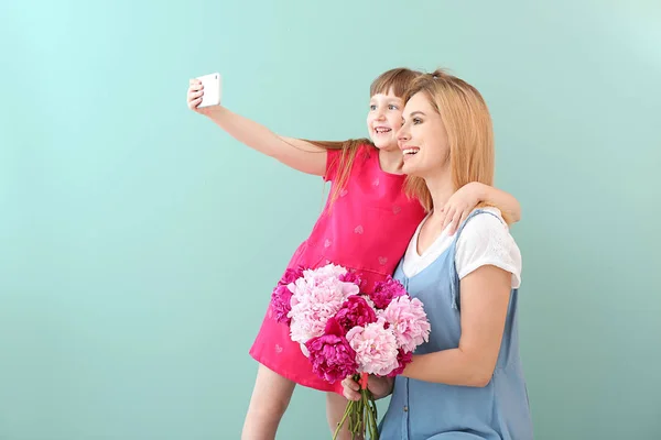 Holčička a její matka si berou na barevné pozadí květiny. — Stock fotografie
