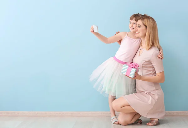 Little girl and her mother taking selfie with gift near color wall — Stock Photo, Image