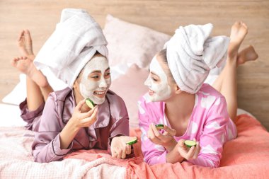 Evde yüz maskeleri ve salatalık dilimleri ile güzel genç kadınlar