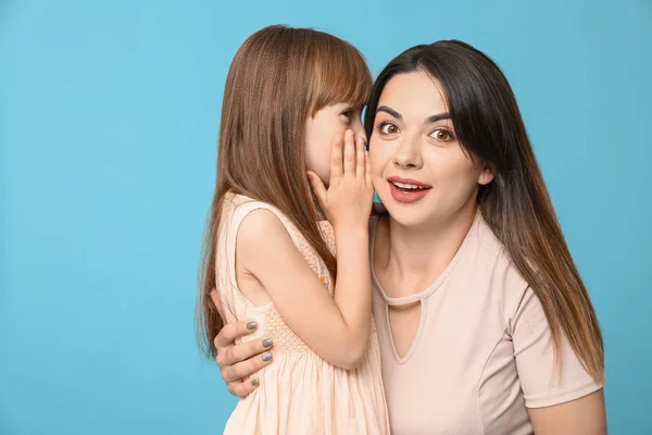 Little girl telling mother her secret against color background — Stock Photo, Image