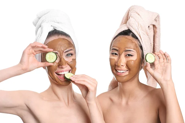 Mulheres bonitas com máscaras faciais e fatias de pepino no fundo branco — Fotografia de Stock