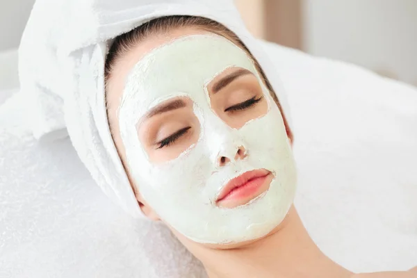 Hermosa mujer joven en tratamiento con mascarilla facial en salón de belleza —  Fotos de Stock