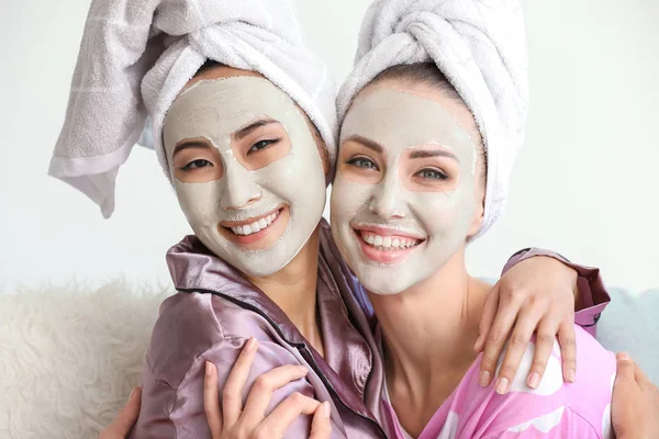 Beautiful young women with facial masks at home — Stock Photo, Image