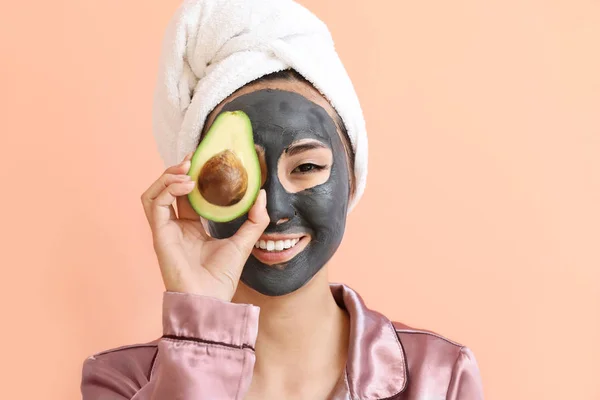 Beautiful Asian woman with facial mask and avocado on color background — Stock Photo, Image