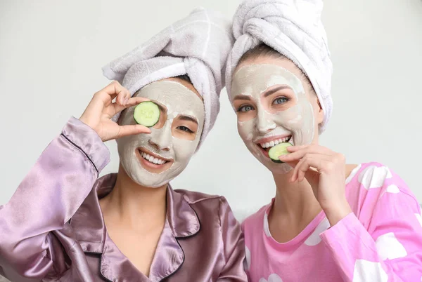 Hermosas mujeres jóvenes con máscaras faciales y rodajas de pepino en casa —  Fotos de Stock