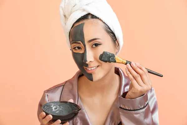 Mooie Aziatische vrouw met gezichtsmasker op kleur achtergrond — Stockfoto