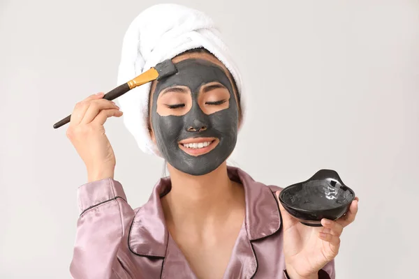 Hermosa mujer asiática aplicando mascarilla facial contra fondo claro — Foto de Stock