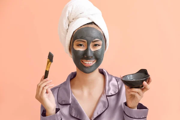 Mooie Aziatische vrouw met gezichtsmasker op kleur achtergrond — Stockfoto