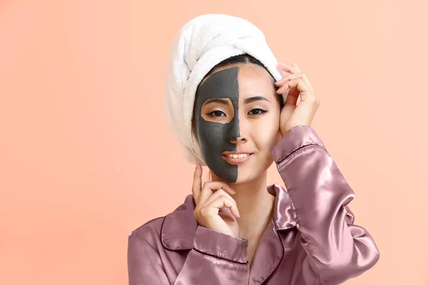 Mooie Aziatische vrouw met gezichtsmasker op kleur achtergrond — Stockfoto