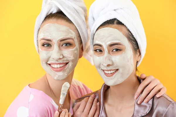 Belle giovani donne con maschere facciali su sfondo di colore — Foto Stock