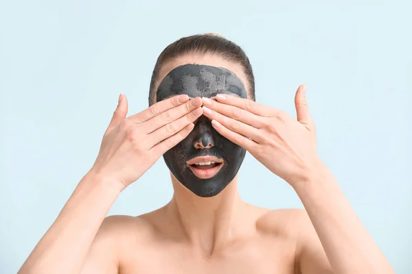 Mooie jonge vrouw met gezichtsmasker op kleur achtergrond — Stockfoto