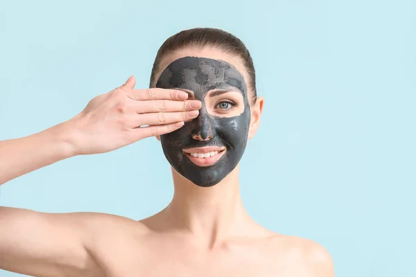 Mooie jonge vrouw met gezichtsmasker op kleur achtergrond — Stockfoto