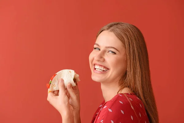 Woman eating tasty taco on color background