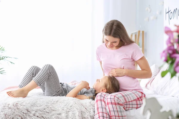 Hermosa mujer embarazada con su hija pequeña en el dormitorio — Foto de Stock