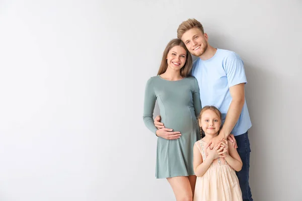 Schöne schwangere Frau mit ihrer Familie auf hellem Hintergrund — Stockfoto