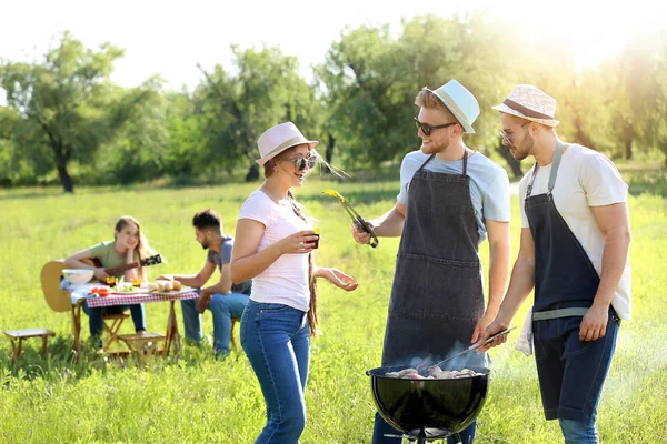 Přátelé vaříte chutné pokrmy na grilu venku — Stock fotografie