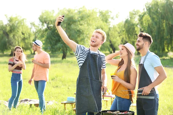 Friends taking selfie while cooking tasty food on barbecue grill outdoors — Stock Photo, Image