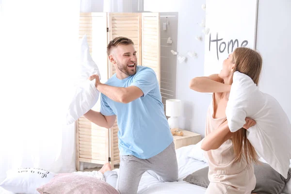Портрет счастливой молодой пары, сражающейся подушками в спальне — стоковое фото