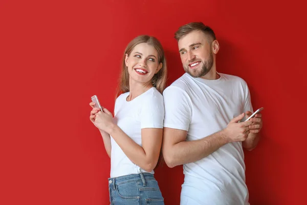 Retrato de jovem casal feliz com telefones celulares em fundo de cor — Fotografia de Stock