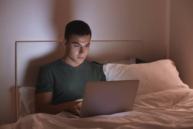 Gece yatakta dizüstü bilgisayar ile genç adam