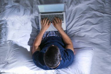 Gece yatakta dizüstü bilgisayar ile genç adam, üst görünümü