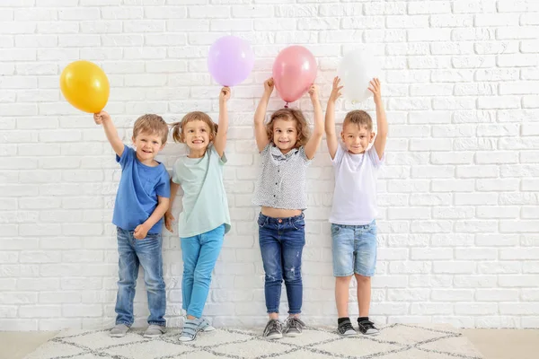 Śliczne małe dzieci z balonami w pobliżu białego muru ceglanego — Zdjęcie stockowe