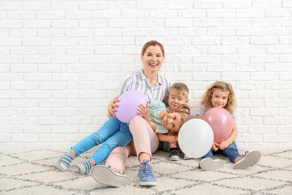 Schattige kleine kinderen met kleuter leraar en lucht ballonnen zitten in de buurt van witte bakstenen muur — Stockfoto