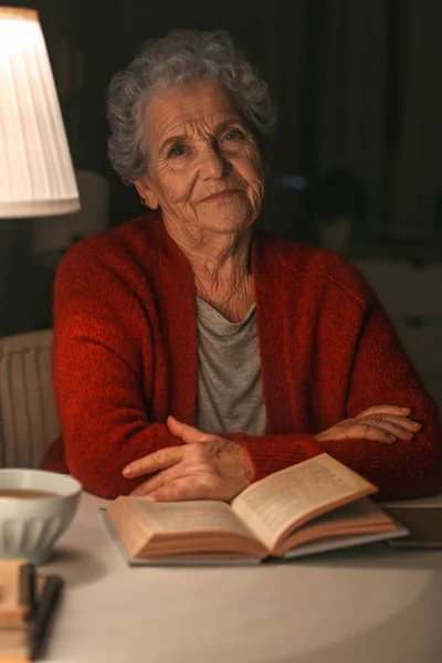 Senior woman reading book at night — Stock Photo, Image