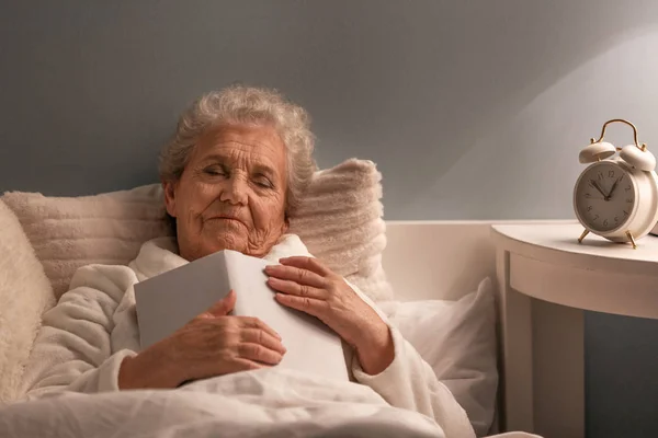 Старша жінка з книгою спить в ліжку вночі — стокове фото