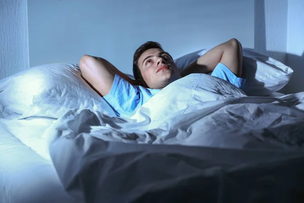 Joven que sufre de insomnio mientras está acostado en la cama por la noche — Foto de Stock