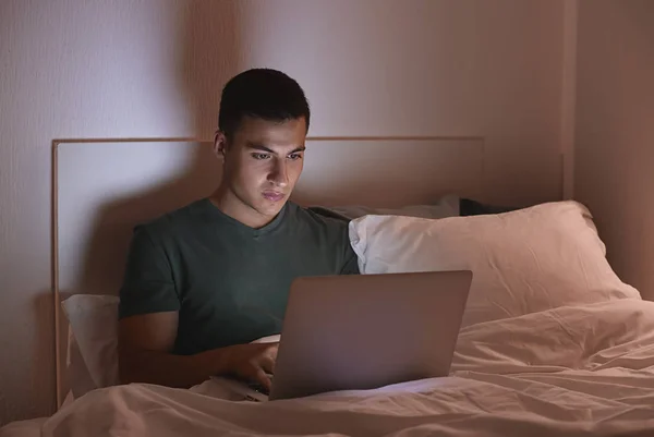 Young man with laptop in bed at night — Stock Photo, Image