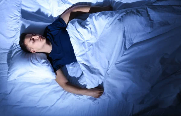Молодой человек спит в постели ночью — стоковое фото