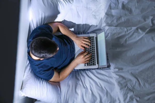 Young man with laptop in bed at night, top view — Stock Photo, Image