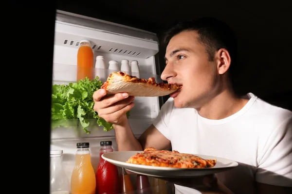 Young man eating pizza near refrigerator at night — Stock Photo, Image