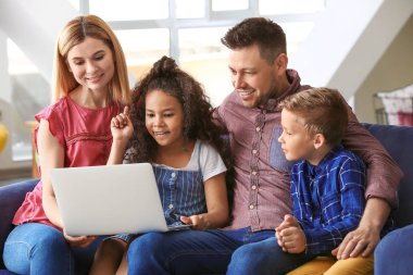 Evde dizüstü bilgisayar kullanan küçük evlatlık çocukları ile Mutlu çift