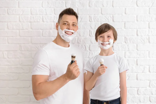 Ο πατέρας και ο μικρός γιος του με αφρό ξυρίσματος σε πρόσωπα από λευκό τοίχο τούβλων — Φωτογραφία Αρχείου