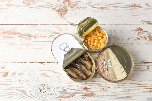 Latas de lata com alimentos diferentes em fundo de madeira branca — Fotografia de Stock