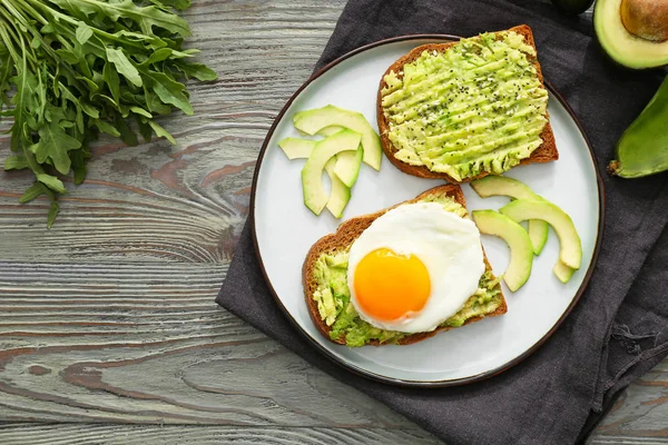 Ahşap masa üzerinde lezzetli avokado tost ile Plaka — Stok fotoğraf