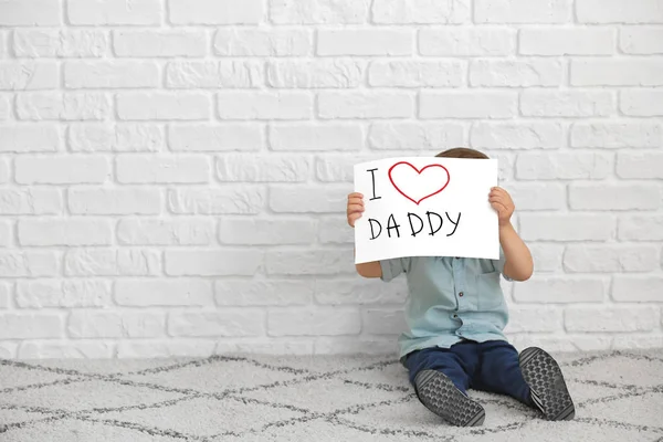 Lindo niño con tarjeta de felicitación para el Día del Padre cerca de la pared de ladrillo blanco — Foto de Stock