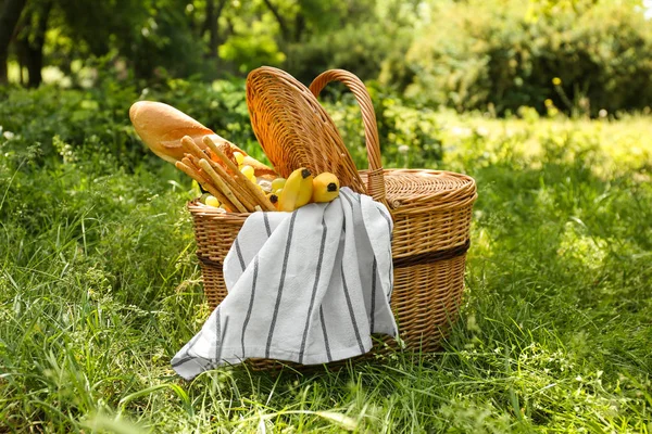 Wicker basket with tasty food and drink for romantic picnic in park — Stock Photo, Image